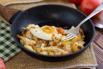 fried omelette with cauliflower and vegetables in a frying pan on a wooden table