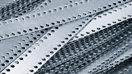 Fototapeta premium A pile of metal pieces with holes in them. Blue holes are of different sizes and shapes. The metal pieces are arranged in a way that they form a pattern. Concept of order and structure