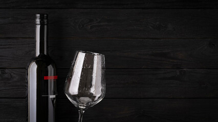 bottle of wine and wine glass on dark wooden background with copy space