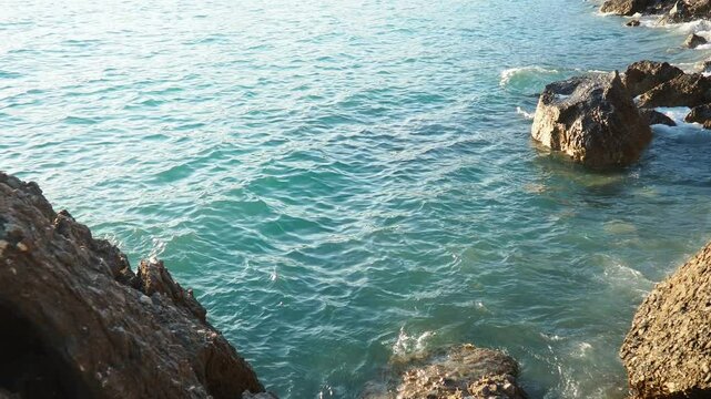 Waves gently lap at rocky shore during stunning sunset over ocean. Golden sunlight reflects off waves as they roll onto shore, creating tranquil atmosphere at sunset by sea. Montenegro summer, Canj
