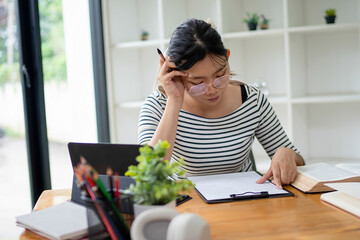 Intelligent young woman having online lessons on laptop, drinking coffee and taking notes,