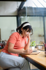 Intelligent young woman having online lessons on laptop, drinking coffee and taking notes,