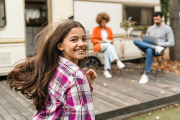 Daughter kid child playing running on yard porch of motor wheel van home while parents working remotely with laptop. Travelling trip adventures voyage by trailer