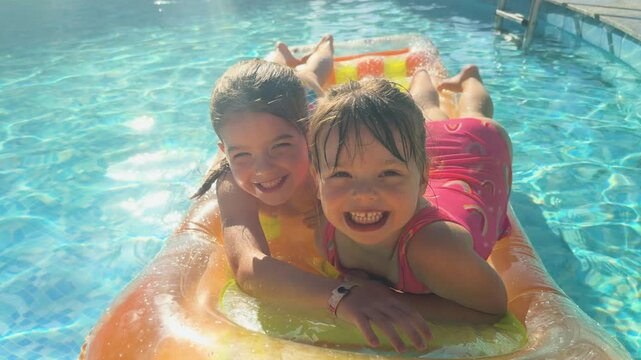 4K: Two young girls smiling at the camera lying on an Inflatable Lilo in the Swimming pool on Vacation Holiday. Stock Video Clip Footage
