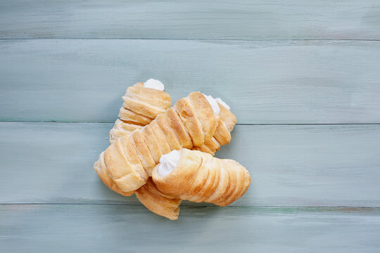 Stack of flaky puff pastry cream horns, Cannoncini, filled with vanilla cream on rustic table.  Selective focus with blurred background.