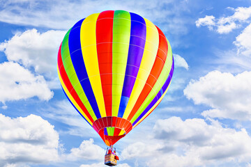 Colorful hot air balloon flying over blue sky with white clouds	