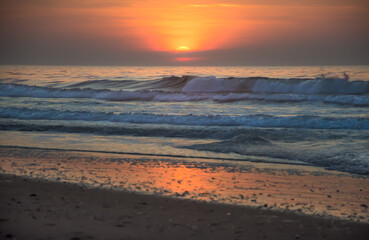 Colorful, early morning sunrise over the Atlantic Ocean, North Myrtle Beach, SC, with breaking waves and sun reflecting on sandy beach.