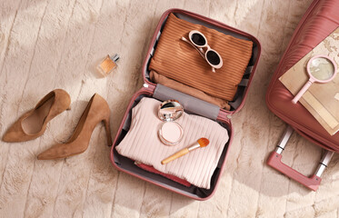 Suitcase with female clothes and accessories on white blanket. Vacation and travel concept.