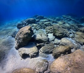 Rocky underwater seascape in the shallow sea, blue water and sun light. Travel photo from scuba diving trip, seabed and stones. Sun, sand, vivid blue water.