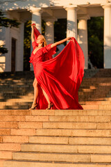 A woman in a long red dress against the backdrop of sunrise, bright golden light of the sun's rays. The concept of femininity, harmony.