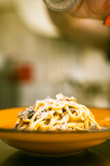 Fresh pasta topped with grated cheese on a vibrant yellow plate. Perfect for Italian restaurant menus, highlighting rich flavors and visually appealing plating.