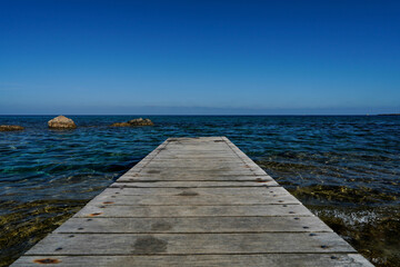 Obraz premium Wallpaper of Charming Wooden Dock on a Rocky Shoreline with Turquoise Sea Waves