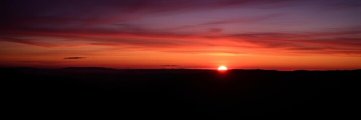 A serene landscape with a deep purple sky, silhouetted trees, and a glowing sun setting behind distant mountains, outdoor, serene