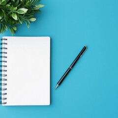 Notebook, pen, and plant on a vibrant blue table, ideal for creative work.