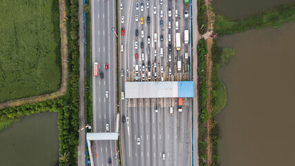 Obraz premium Aerial view of a bustling city expressway toll gate, featuring multiple lanes filled with vehicles waiting in line for fee payment.