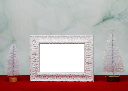 White vintage photo frame with Christmas tree on red table and marble background.Christmas concept.