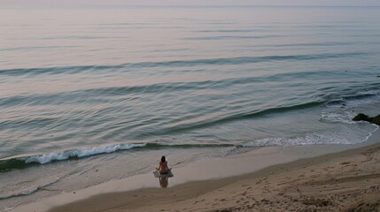 A lone figure sits quietly by the sea, absorbing the calmness of the gentle waves in the serene morning light.