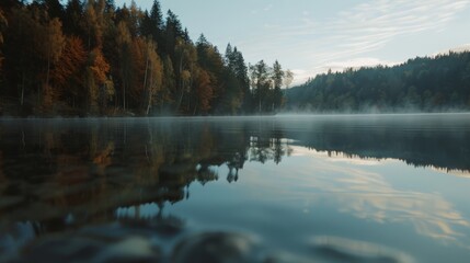 Calm lake mirrors autumn trees in a peaceful setting, as early mist rises, creating an ethereal blend of earth, water, and sky.