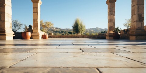 Obraz premium A low angle view of a stone patio with pillars on either side, a blurred background of a tree and distant hills, and terracotta pots with plants
