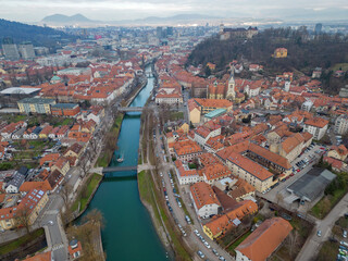 Ljubljana city aerial view above Ljubljanica river from Trnovski pristan towards city center and historic town with the castle. Cloudy day in the winter. Boat with tourists on a river cruise.