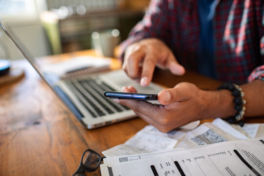 Stressed man looking at laptop with bills on tablet at kitchen