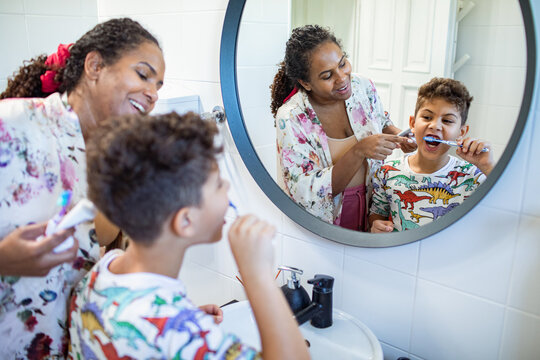 Mother and son brushing teeth together in bathroom mirror