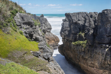 Two steep cliffs with a gap in-between with sea water rushing in.