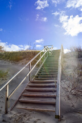 a set of steps leading up to a beach with a blue sky and clouds.