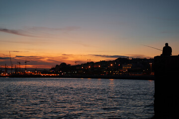 Fototapeta premium Silhouette of people on the Tejo river bank in Lisbon at sunset