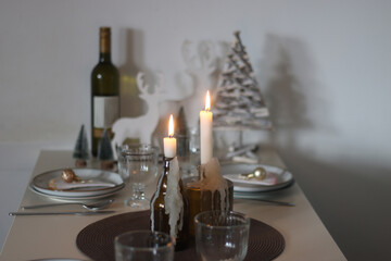 Table set for Christmas meal with plates, glasses, holiday decorations, lit candles and wine. Selective focus.