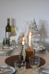 Table set for Christmas meal with plates, glasses, holiday decorations, lit candles and wine. Selective focus.
