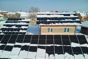 Aerial view of snow melting from covered solar photovoltaic panels installed on house rooftop for...