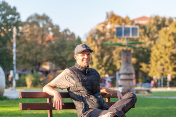 A cheerful man is sitting alone in the park on the bench and enjoying the autumn sun