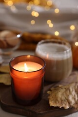 Burning candle and dry leaf on light table, closeup. Autumn atmosphere