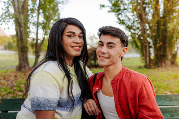 Happy latin transgender couple smiling and relaxing outdoors on park bench