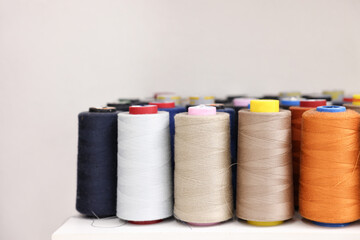 Many different spools of thread on white shelf in professional workshop