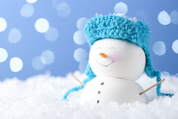 Cute decorative snowman on artificial snow against light blue background with blurred lights,...