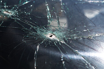 Bullet hole in glass - real bullet hole closeup. Broken car windshield with cracks.
