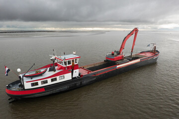 Red dredging vessel working on sea, removing sediment in a waterway