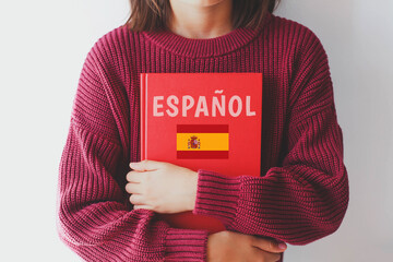 one girl schoolgirl in burgundy sweater holds red spanish language textbook with spain flag and...