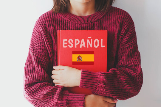 one girl schoolgirl in burgundy sweater holds red spanish language textbook with spain flag and text spanish in spanish, foreign language learning concept