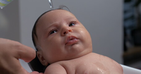 Close-up of a baby being bathed, water gently pouring over the baby’s head, tender and intimate...