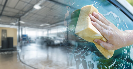 A hand with a washcloth washes a car window.