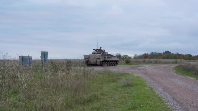 British army Warrior FV510 tracked armoured infantry fighting vehicle moving along a dirt track road