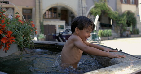 Young boy happily playing in a stone fountain, splashing water while smiling and enjoying the fun...