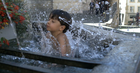 Young boy jumping into water in a public fountain, slow motion at 800 fps, joyful and playful...