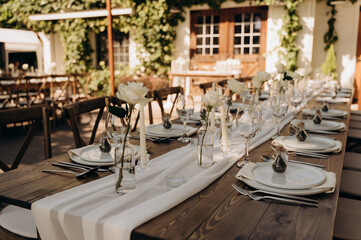 Elegant country-style table setting: white carpet, simple vases with roses on dark wood.