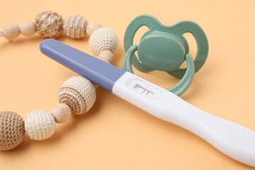 Pregnancy test, pacifier and teether on pale orange background, closeup