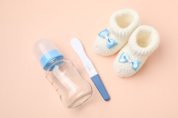 Pregnancy test, feeding bottle and baby booties on beige background, above view