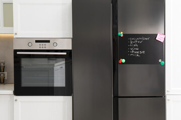 Magnetic board with shopping list and note on refrigerator in kitchen